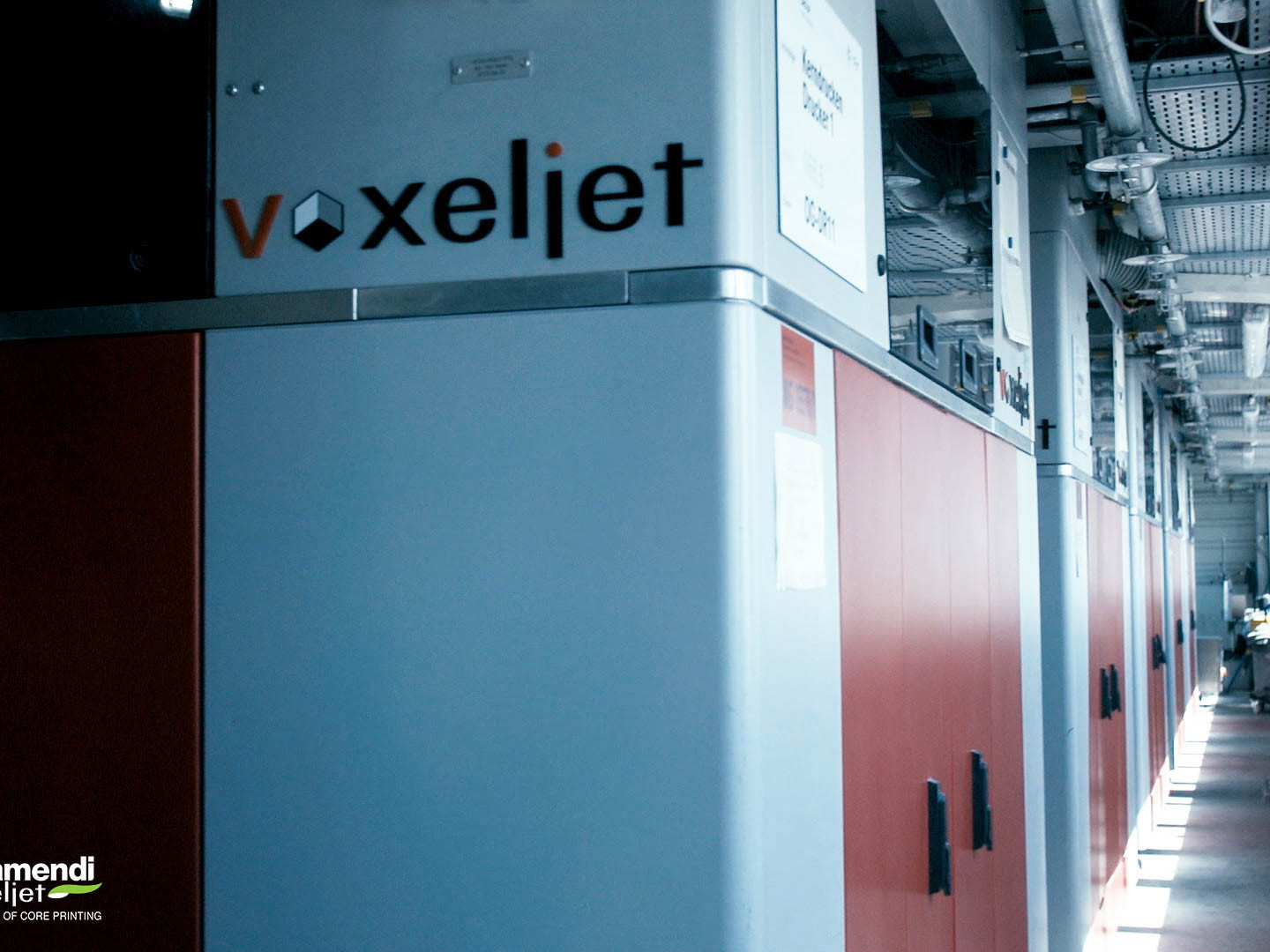 Nahaufnahme einer Seite des 3D-Druckers VX1300 X von voxeljet. zu sehen ist das voxeljet Logo und eine reihe weiterer 3D-Drucker der gleichen Art die in einer Fertigungshalle von BMW installiert sind.