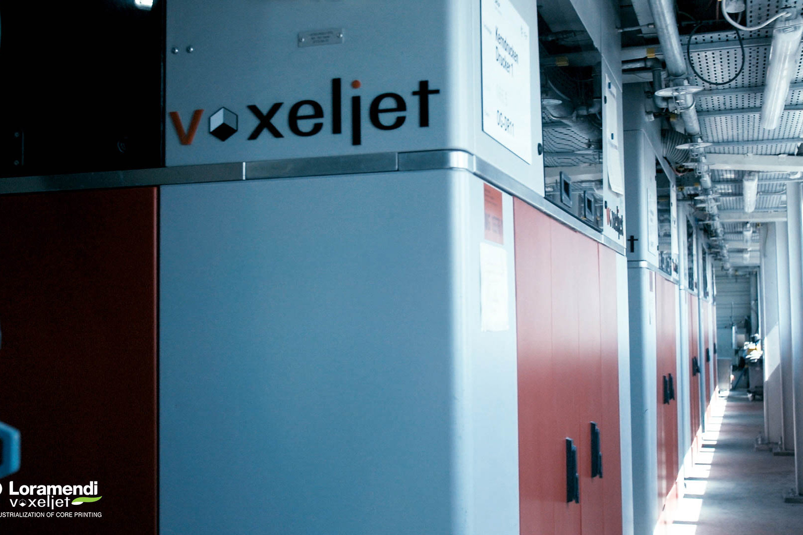 Nahaufnahme einer Seite des 3D-Druckers VX1300 X von voxeljet. zu sehen ist das voxeljet Logo und eine reihe weiterer 3D-Drucker der gleichen Art die in einer Fertigungshalle von BMW installiert sind.