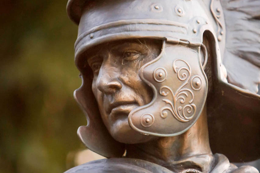 Nahaufnahme einer Bronzeskulptur die einen lebensgroßen römischen Soldaten mit Helm zeigt.