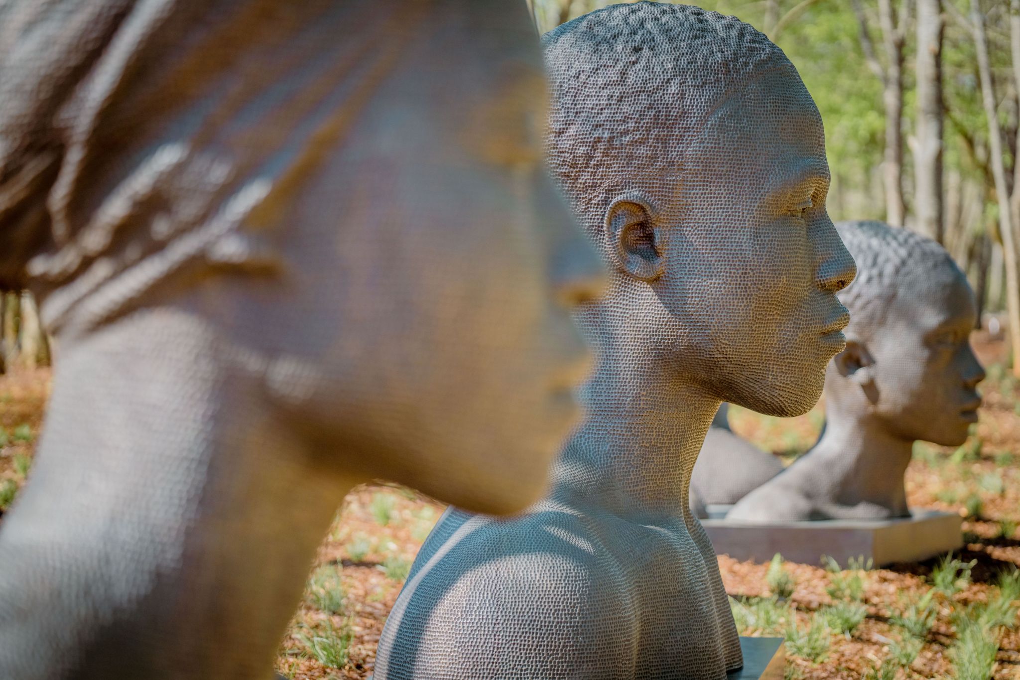 Zwei in einer Reihe stehenden, aus Bronze gegossene Büsten die mit 3D-Druck und Sandguss hergestellt wurden stehen in einer Reihe und werden vom Profil aus betrachtet.